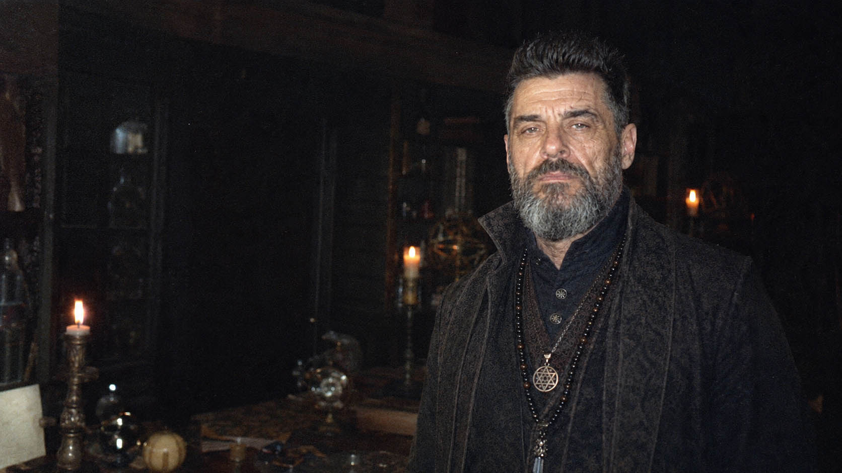 Victor Draconic witchcraft practitioner in a dark candlelit ritual chamber with an open occult manuscript and spellcasting tools